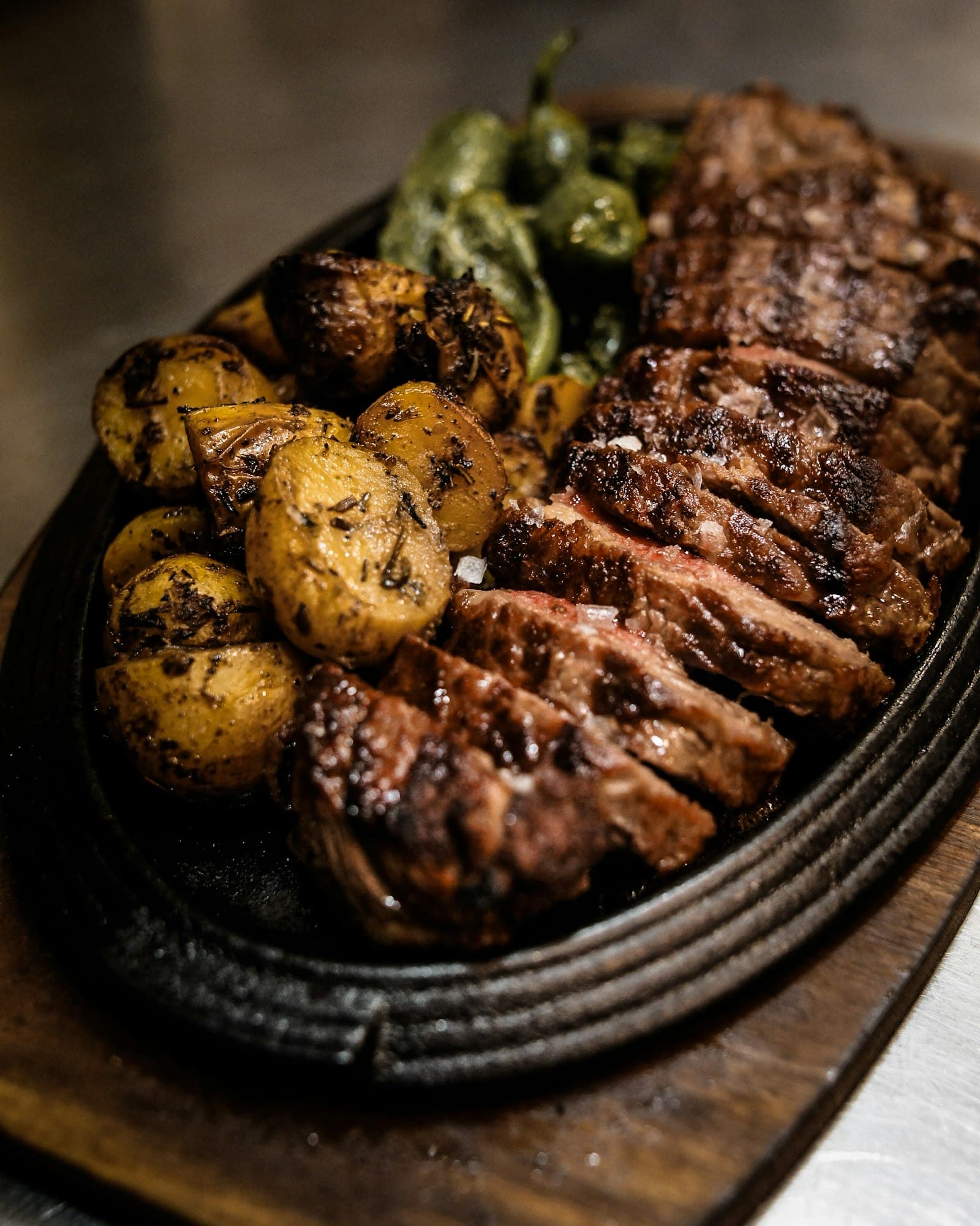 Sliced flame-grilled rump on a sizzling cast-iron platter with roast potatoes