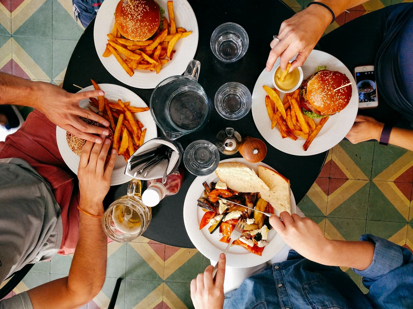 A full table seen from above — prego rolls, chips and cold drinks on patterned tiles