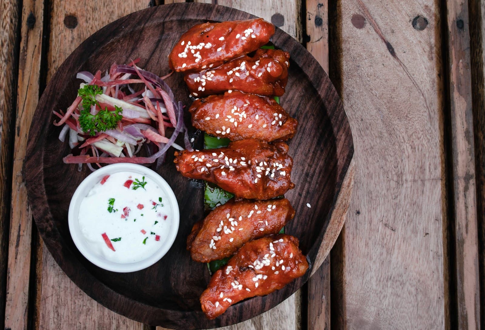 Chicken wings glazed in red peri-peri sauce on a dark wooden board